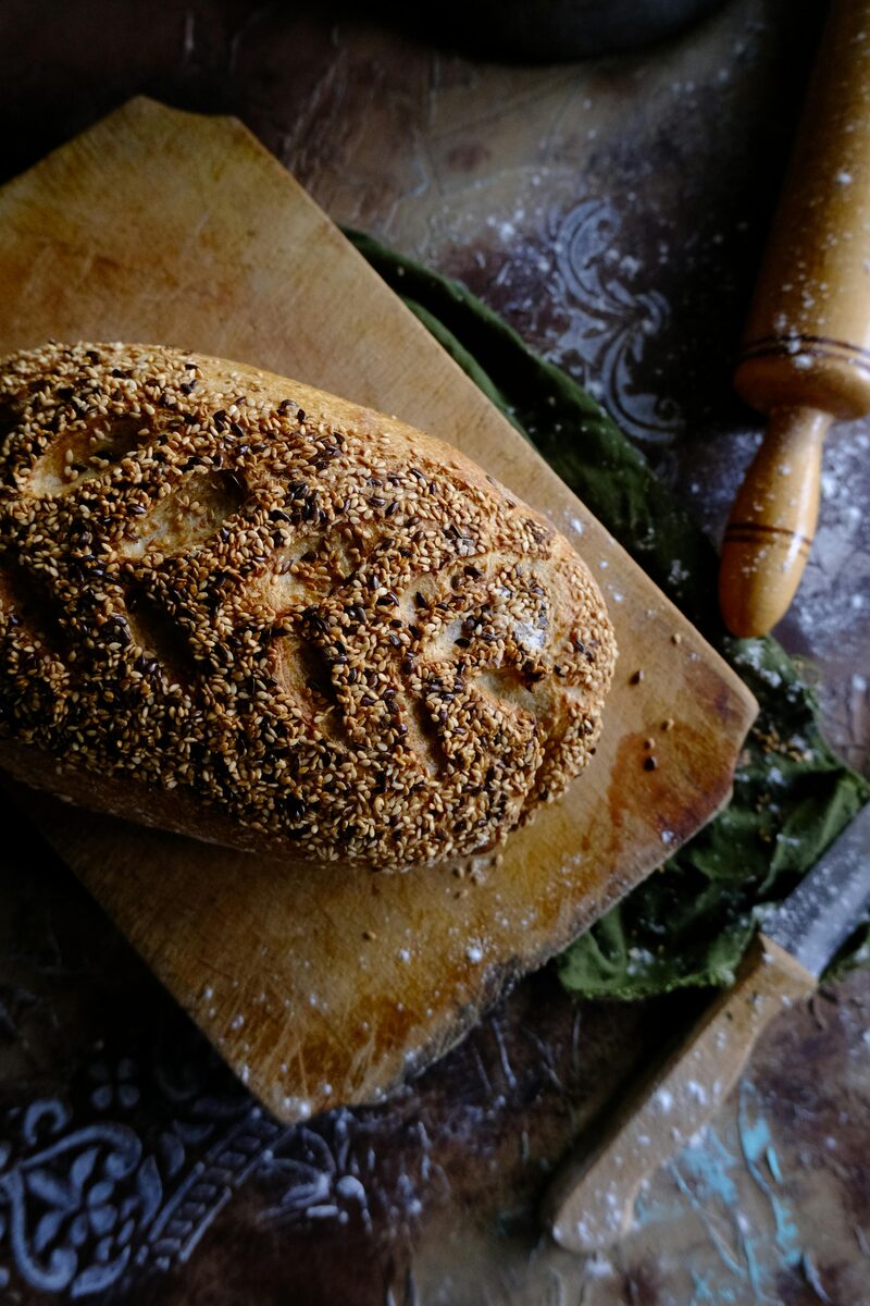 A seeded artisan loaf on a wooden board with a rolling pin