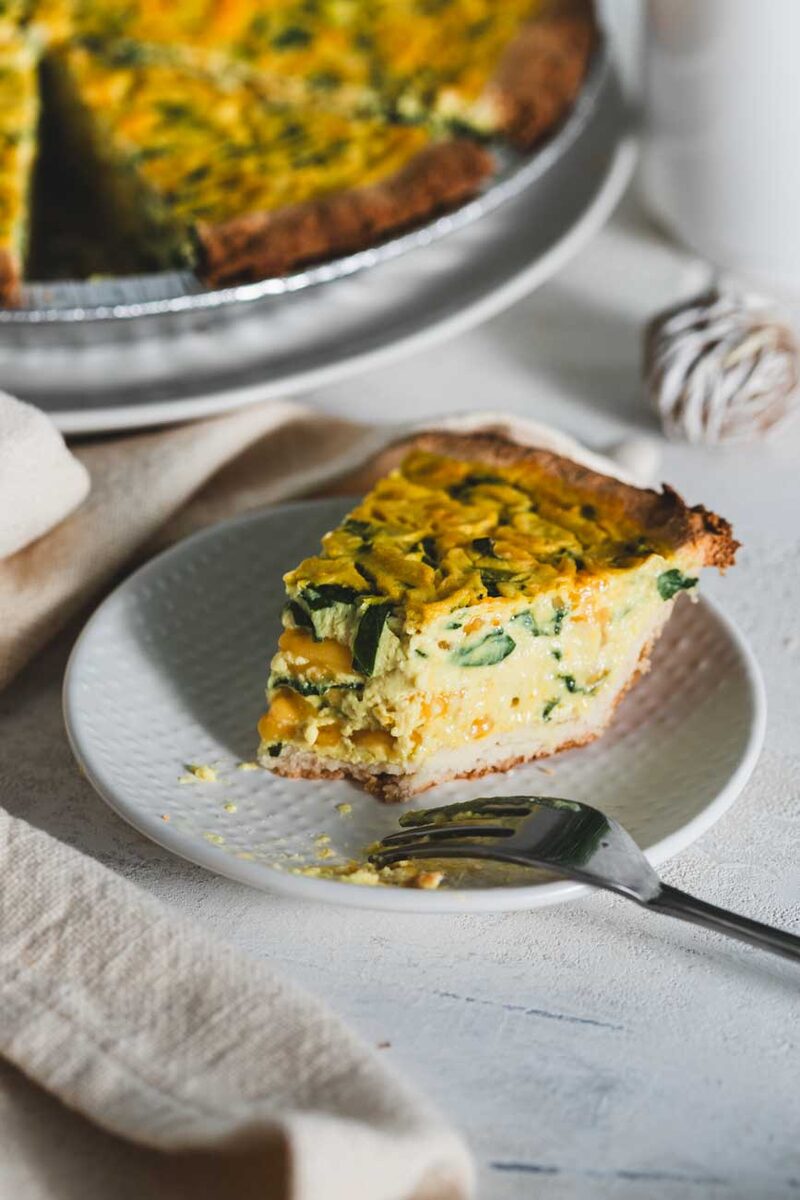 A slice of spinach cheddar quiche on a plate with a fork