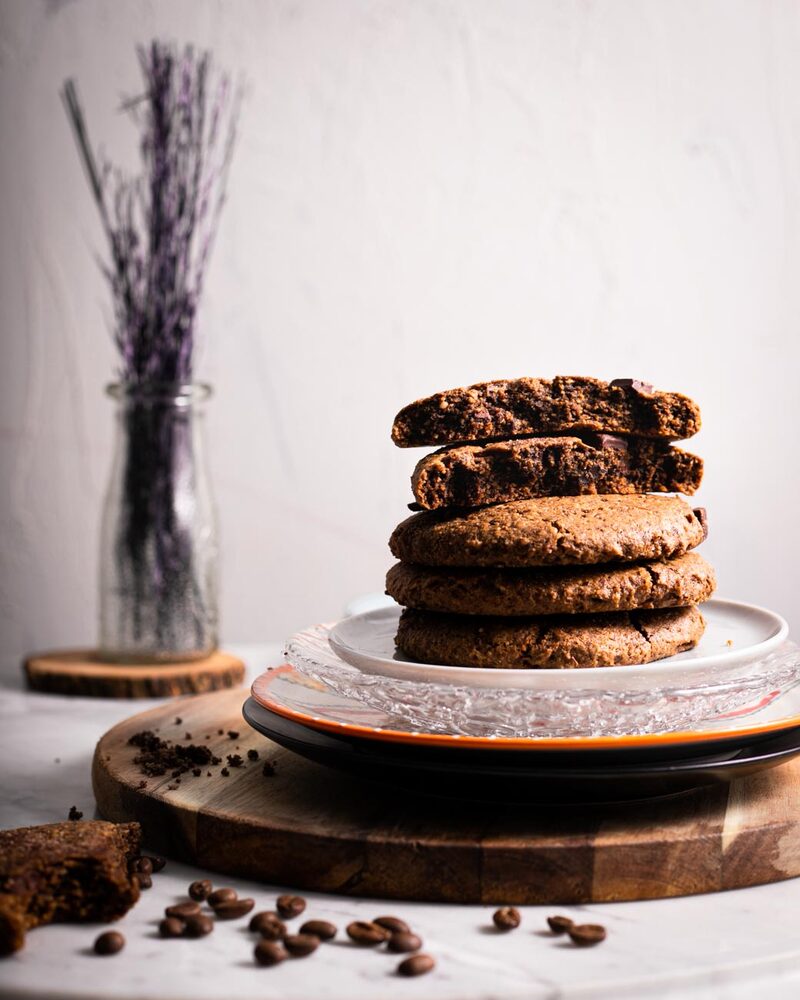 Stack of deeply browned chocolate chunk cookies on a glass plate with coffee beans scattered around