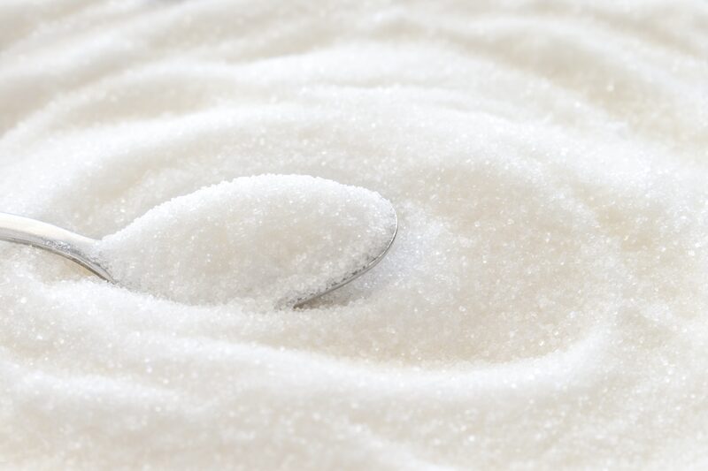 A spoonful of white granulated sugar resting on a pile of sugar