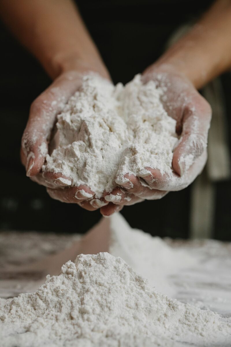Baker's hands cupping a mound of fine white flour over a floured worktable