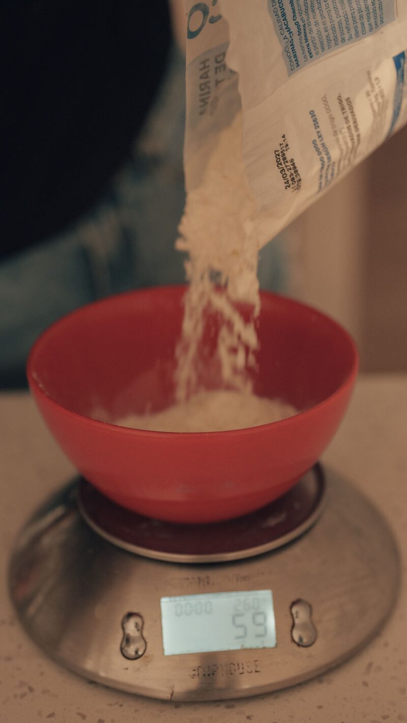 Flour being poured from a bag into a bowl on a digital kitchen scale