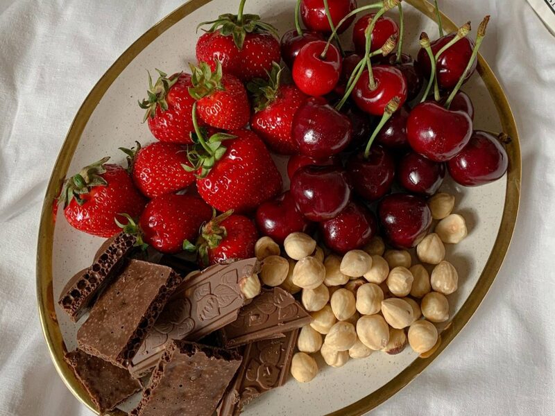 A plate of chocolate chunks, hazelnuts, cherries, and strawberries