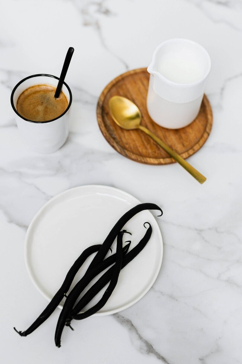 A plate of dried vanilla beans on a white counter with cups of coffee