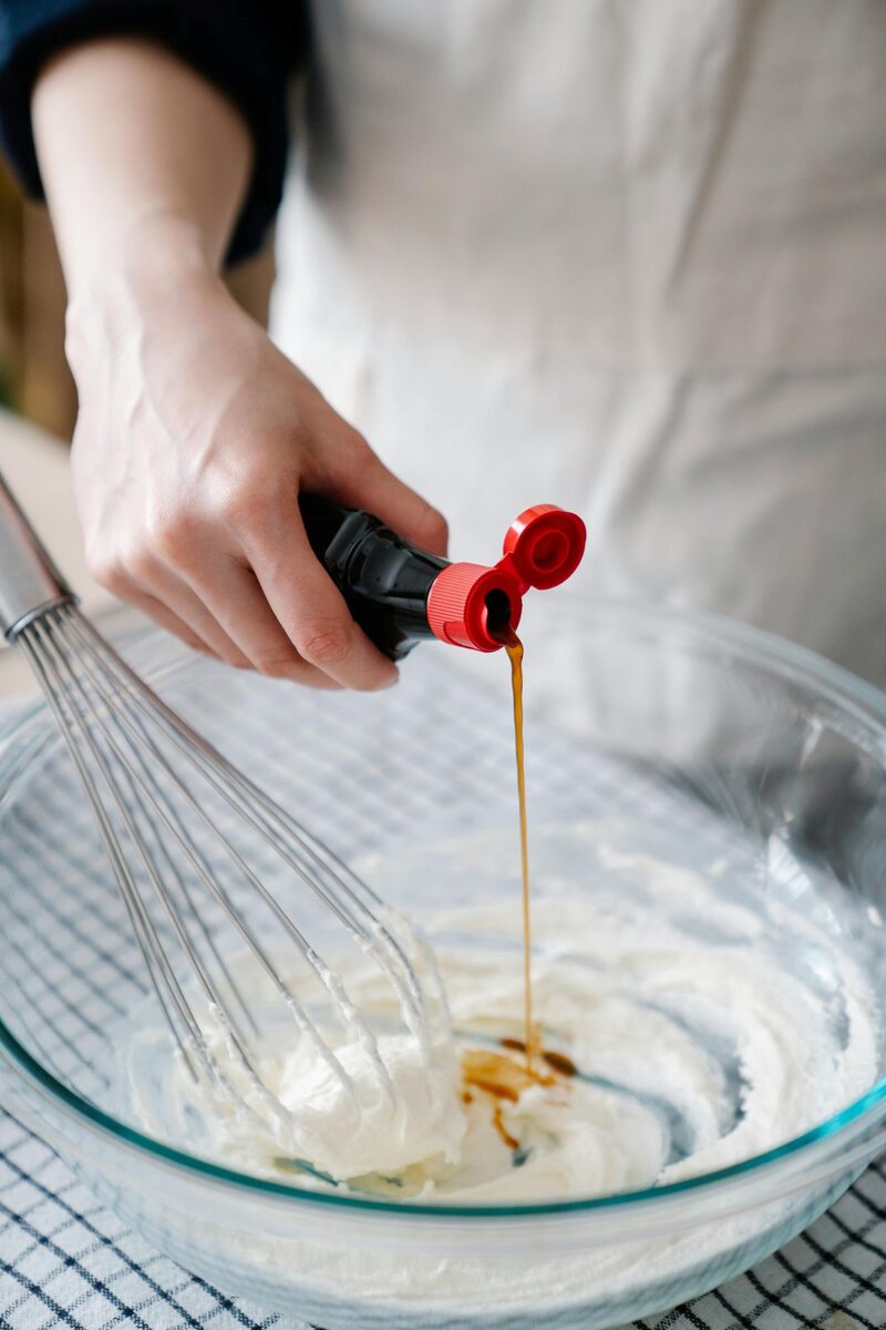 A baker pouring vanilla paste into a bowl of ingredients