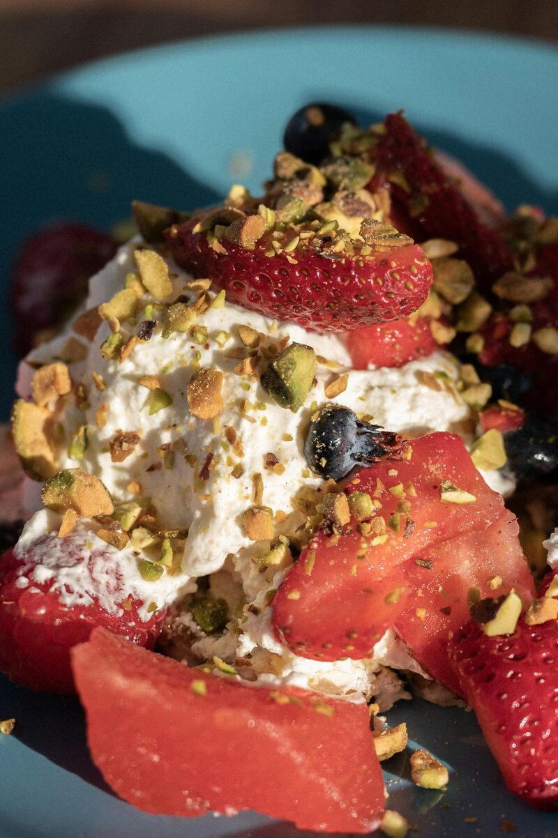 Whipped vegan cream with fresh strawberries, blueberries, and crushed pistachios on a plate