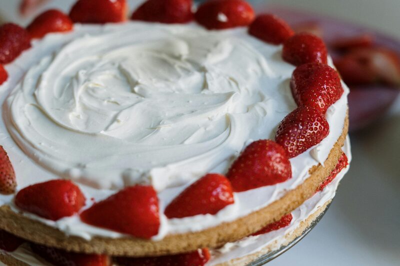 A layered sponge cake topped and filled with whipped vegan cream and fresh strawberries