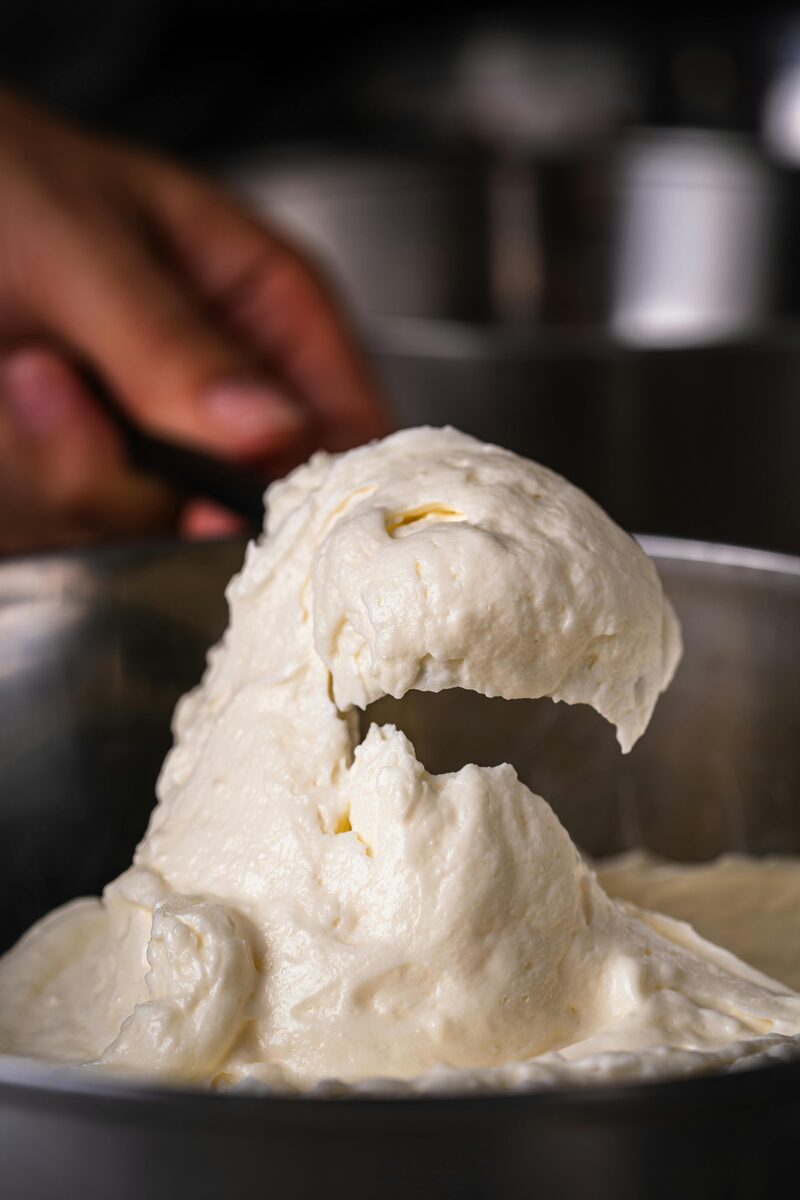 Stiff peaks of whipped vegan cream lifted on a whisk from a mixing bowl