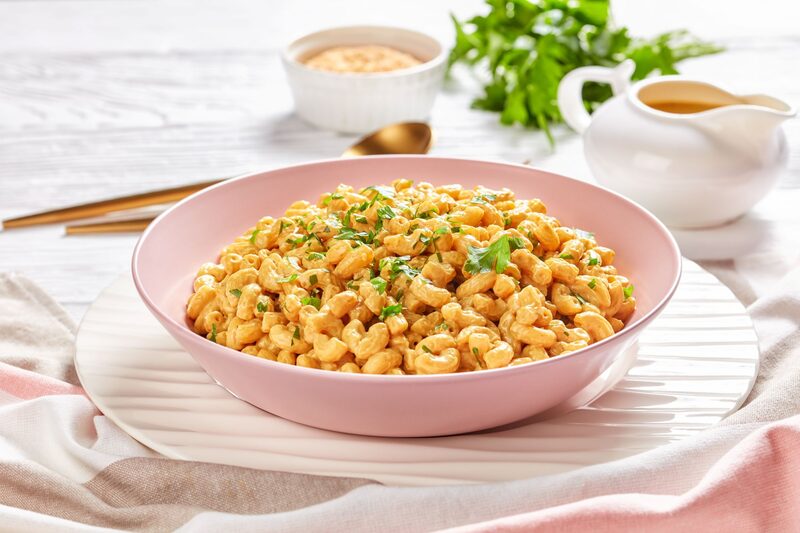 A pink bowl of creamy vegan mac and cheese garnished with parsley