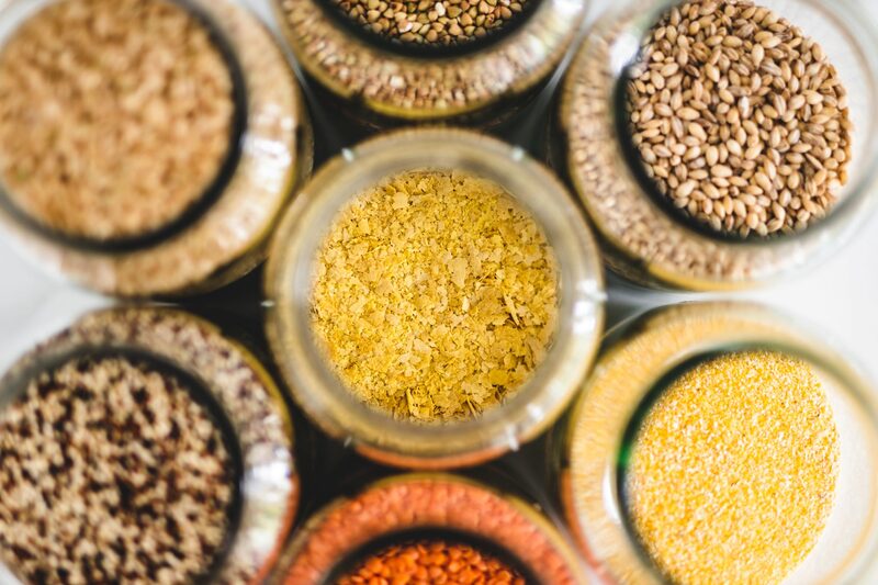 Top-down view of jars holding nutritional yeast flakes alongside grains and lentils